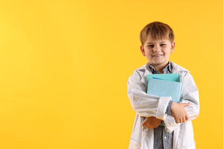 Smiling little boy in laboratory coat with books on yellow background, space for text. Child and scienceの写真素材