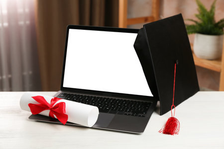 Diploma, graduation cap and laptop on white wooden table indoors, closeupの写真素材