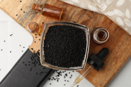 Black cumin seeds in bowl, pipette and bottles of essential oil on white table, flat layの写真素材