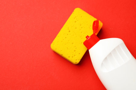 Kitchen sponge and dish soap on red background, top view. Space for textの写真素材