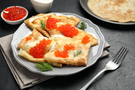 Tasty crepes with red caviar and sour cream on black textured table, closeupの写真素材