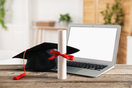 Diploma, graduation hat and laptop on wooden table indoors, selective focusの写真素材