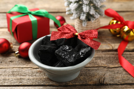 Pieces of black coal in bowl and Christmas decor on wooden table, closeupの写真素材
