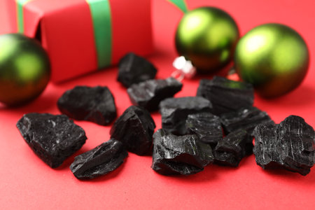 Pieces of black coal, gift box and Christmas baubles on red background, closeupの写真素材