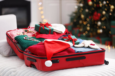 Christmas vacation. Suitcase with Santa hat, clothes, gift boxes and candy canes indoors, closeupの写真素材