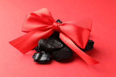Pieces of black coal with bow on red background, closeup. Christmas tradition for kidsの写真素材