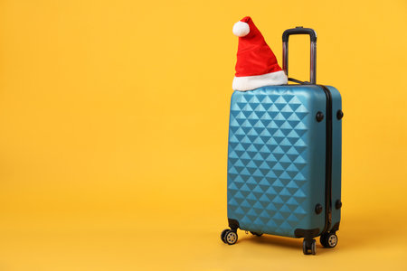 Santa hat on blue suitcase against orange background, space for text.の写真素材