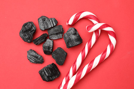 Pieces of black coal and candy canes on red background, flat layの写真素材