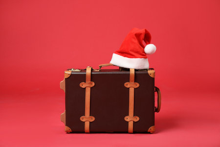 Christmas vacation. Stylish suitcase and Santa hat on red backgroundの写真素材