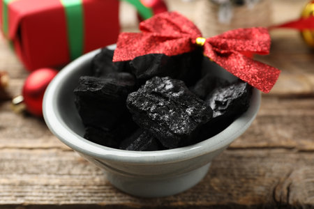 Pieces of black coal in bowl and Christmas decor on wooden table, closeupの写真素材