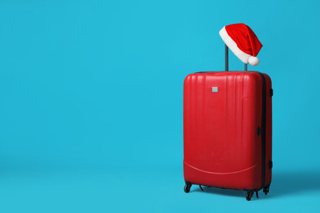 Christmas vacation. Suitcase with red Santa hat on light blue backgroundの写真素材