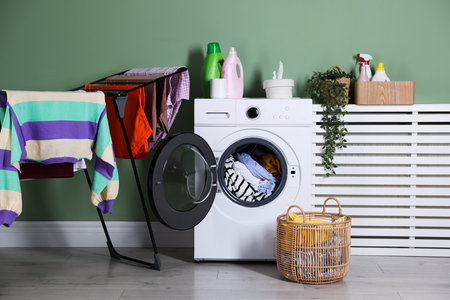 Modern washing machine, detergents, houseplant and clothes near light green wall indoorsの写真素材