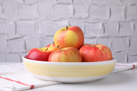 Ripe red apples in bowl on white table near gray textured wall, closeupの写真素材