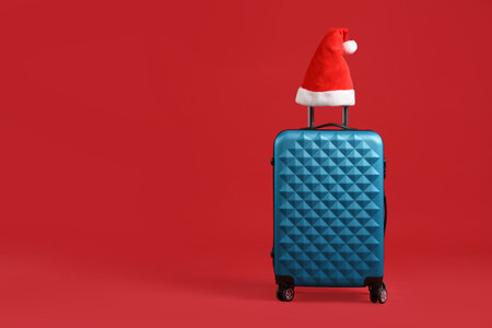 Christmas vacation. Blue suitcase with Santa hat on red background, space for textの写真素材