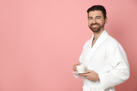 Man in bathrobe with cup of coffee on pink background. Space for textの写真素材