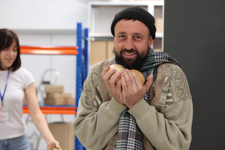 Volunteers helping homeless people in shelter, focus on man with bread