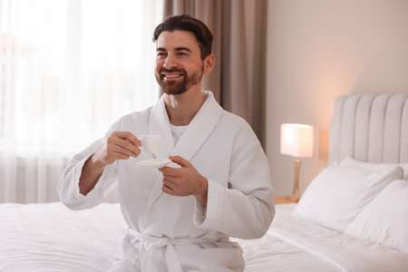 Man in bathrobe with cup of coffee on bed indoorsの写真素材