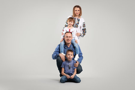 Full-length portrait of happy family in embroidered shirts on light gray background