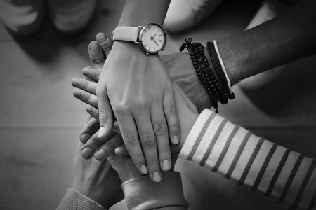 Group of people stacking their hands together, top view. Black-and-white toning