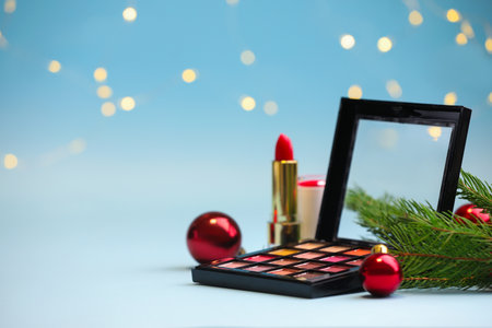 Makeup products and Christmas decor on light blue background with blurred lights, space for text. Bokeh effectの写真素材