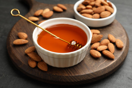 Delicious honey in bowl and almonds on dark textured table, closeupの写真素材