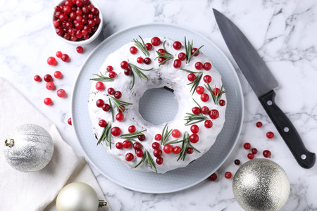Tasty Christmas cake with cranberries, rosemary, baubles and knife on white marble table, flat layの写真素材