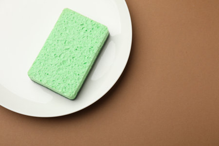 Kitchen sponge and plate on brown background, top view. Space for textの写真素材