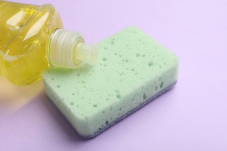Clean kitchen sponge and soap dish on violet background, closeup