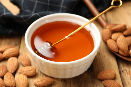 Delicious honey in bowl, dipper, spoon and almonds on wooden table, closeupの写真素材