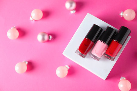 Stylish presentation of nail polishes and Christmas baubles on pink background, flat layの写真素材