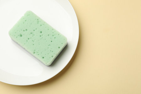 Kitchen sponge and plate on beige background, top view. Space for textの写真素材
