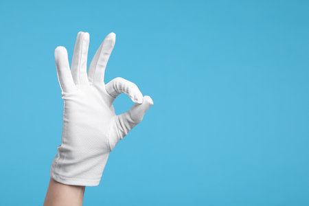 Woman in cloth glove showing okay gesture on light blue background, closeup. Space for textの写真素材