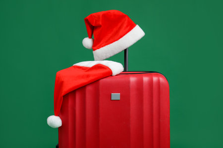 Christmas vacation. Red suitcase with Santa hats on green backgroundの写真素材