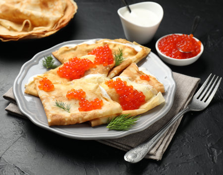 Tasty crepes with red caviar and sour cream on black textured table, closeupの写真素材