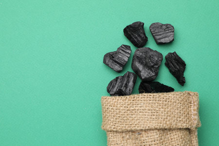 Pieces of black coal in bag on green background, top view. Space for textの写真素材