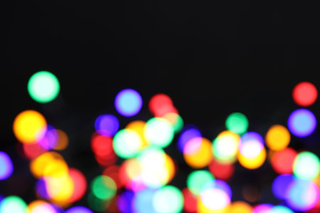 Blurred view of bright Christmas lights on dark background, bokeh effect. Space for text