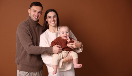Happy parents with their cute baby on brown background. Space for textの写真素材