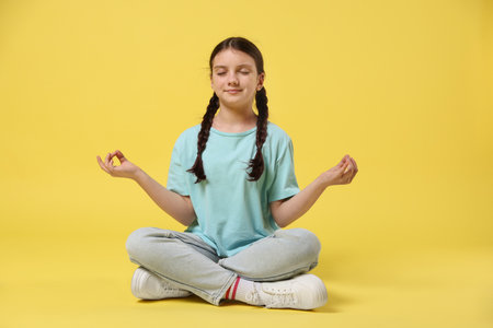 Portrait of cute girl meditating on yellow background