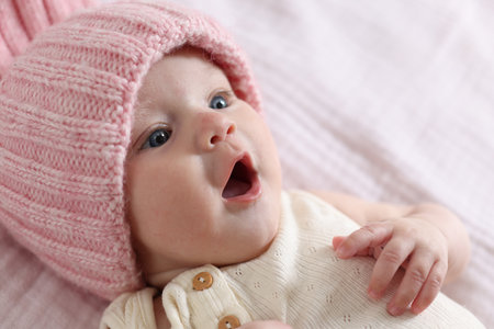 Cute newborn baby in knitted hat on bed