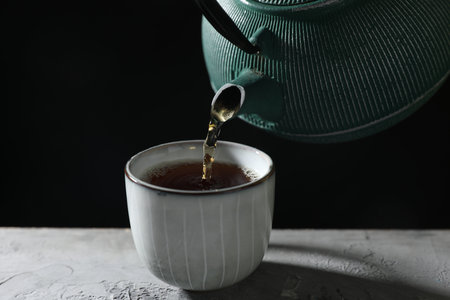 Pouring hot tea into cup from teapot at gray table, closeupの写真素材