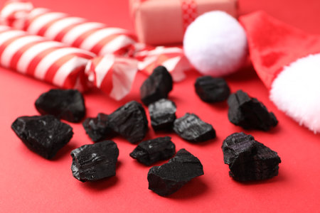 Pieces of black coal, candies, Santa hat and Christmas gift box on red background, closeupの写真素材