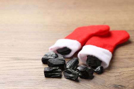 Pieces of black coal in Christmas stockings on wooden table, closeup. Space for textの写真素材