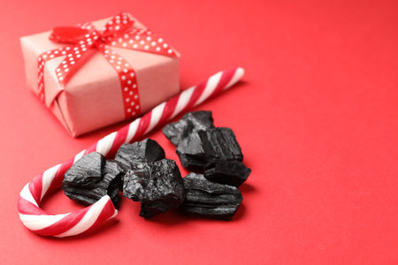 Pieces of black coal, candy cane and Christmas gift box on red background, closeup. Space for textの写真素材