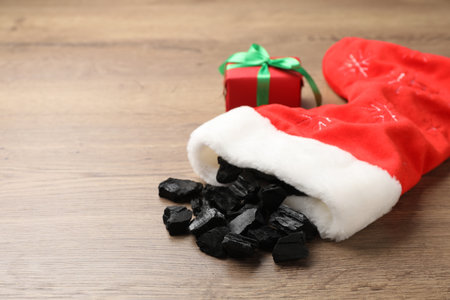 Pieces of black coal in Christmas stocking and festive decor on wooden table, closeup. Space for textの写真素材