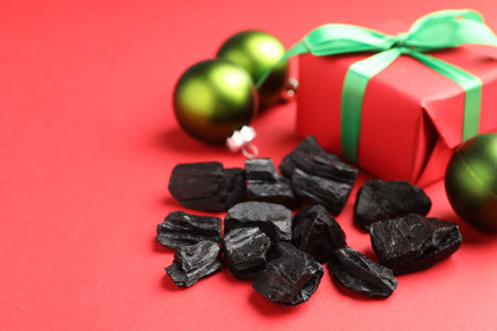 Pieces of black coal, gift box and Christmas baubles on red background, closeupの写真素材