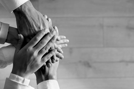Group of people stacking their hands together, top view. Black-and-white toning