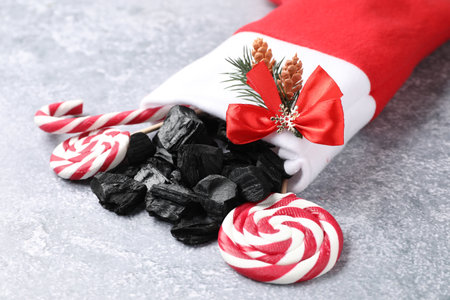 Pieces of black coal, lollipops and candy cane in Christmas stocking on gray textured table, closeup