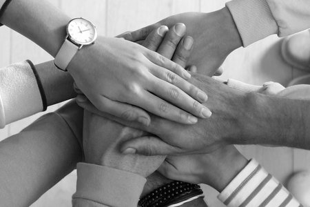 Group of people stacking their hands together, top view. Black-and-white toning