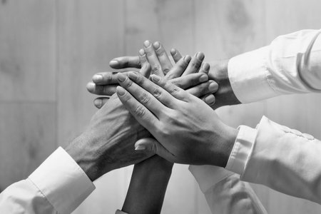 Group of people stacking their hands together, top view. Black-and-white toning