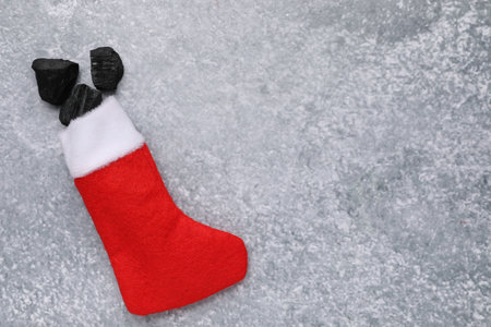 Pieces of black coal in Christmas stocking on gray textured table, top view. Space for textの写真素材